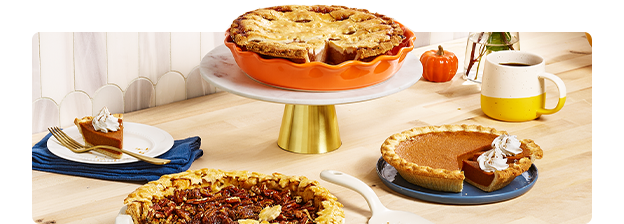 Pumpkin, pecan and apple pies in serving dishes on a countertop.