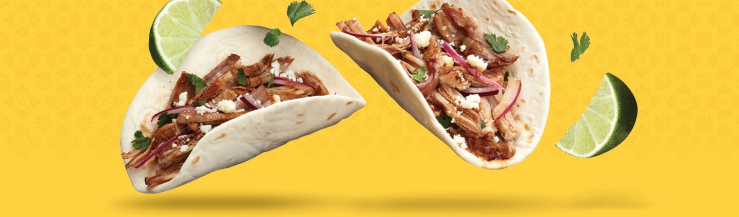 Shredded carnitas soft tacos with lime wedges.