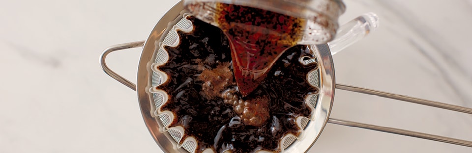 Straining brewed coffee mixture into glass jar.