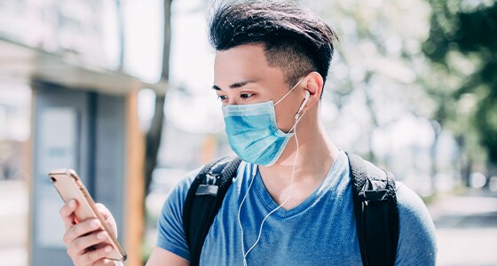 A picture of a young man wearing a sanitary mask and checking his phone A picture of a young man wearing a sanitary mask and checking his phone