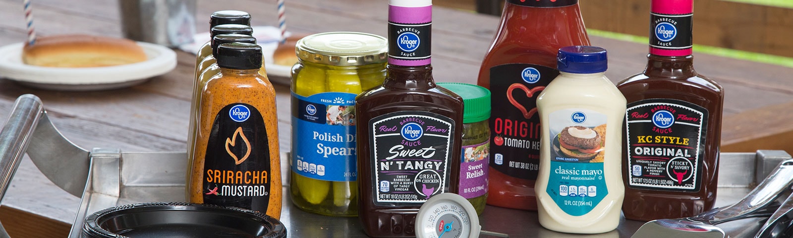 Various condiments sitting on a stainless steel table next to grilling utensils