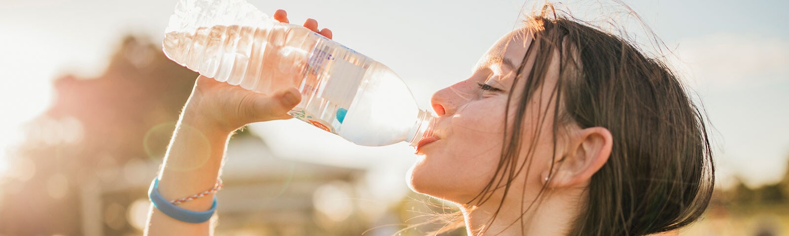 A young female drinking a bottle of water while standing outside A young female drinking a bottle of water while standing outside