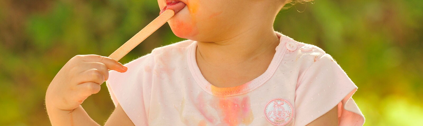 A young girl eating a melted popsicle with stains on her shirt