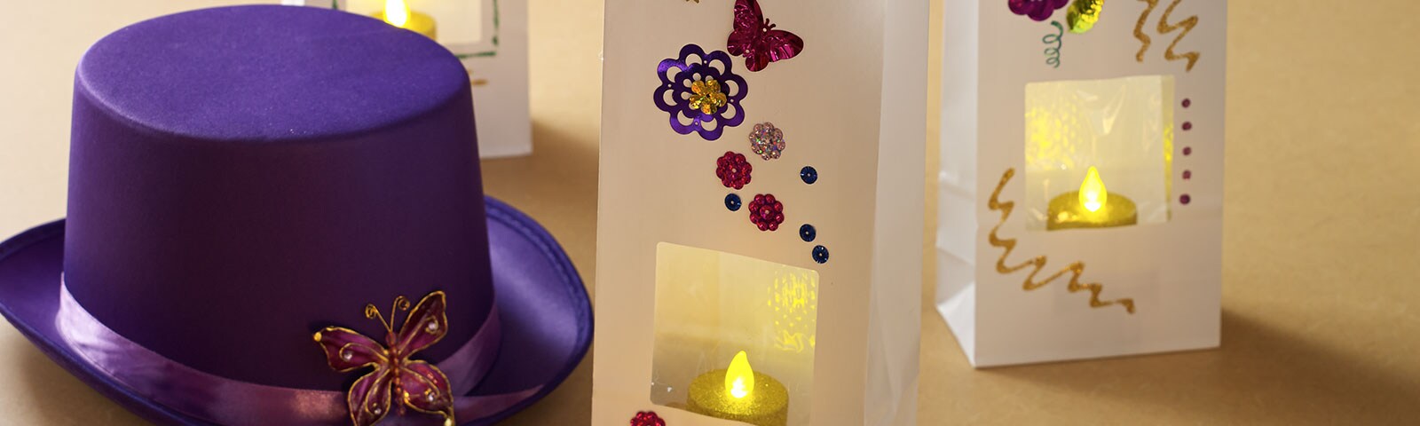 A purple top hat with a decorative brooch along with three white paper bags, decorated and filled with an LED candle