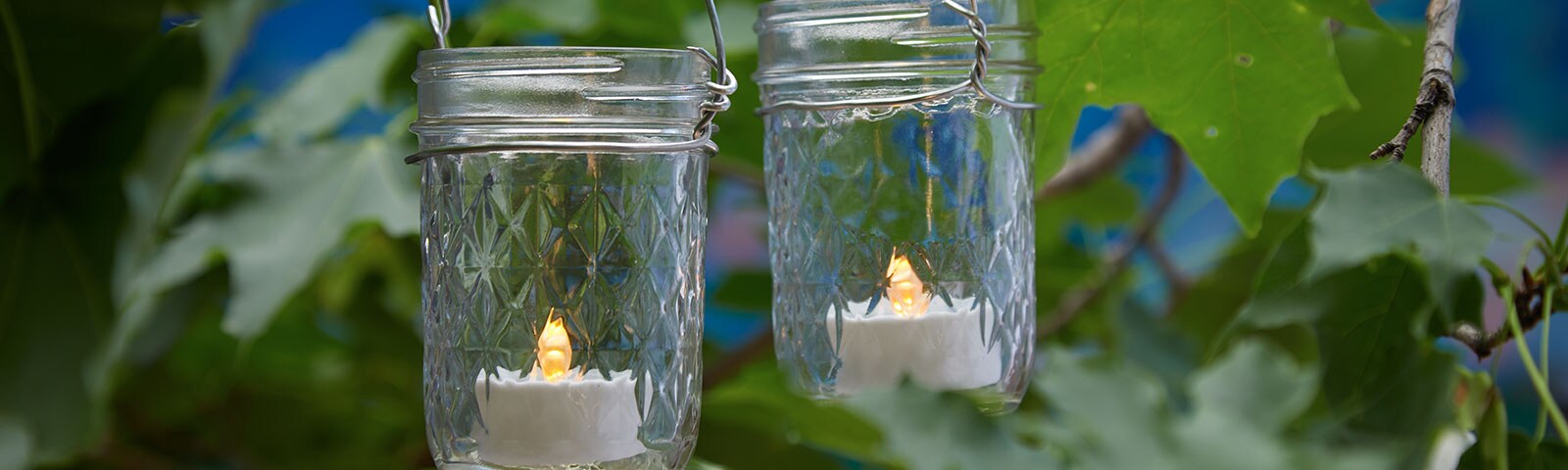 Two mason jars hanging from a tree, each one filled with a small LED candle Two mason jars hanging from a tree, each one filled with a small LED candle