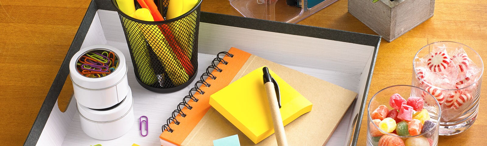 Homemade desk organizer with notepads, pens and paperclips inside next to candy-filled cups on a wooden table Homemade desk organizer with notepads, pens and paperclips inside next to candy-filled cups on a wooden table
