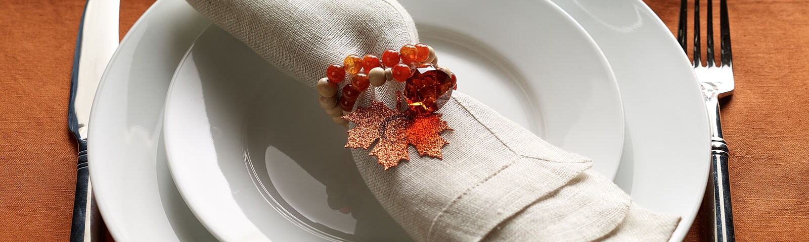 A table setting complete with a knife, fork, salad plate, dinner plate and linen napkin embellished with an ornate autumn napkin ring