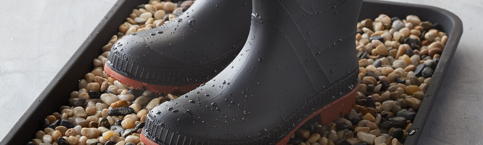 Wet rain boots atop a bed of pebbles sitting in a tray