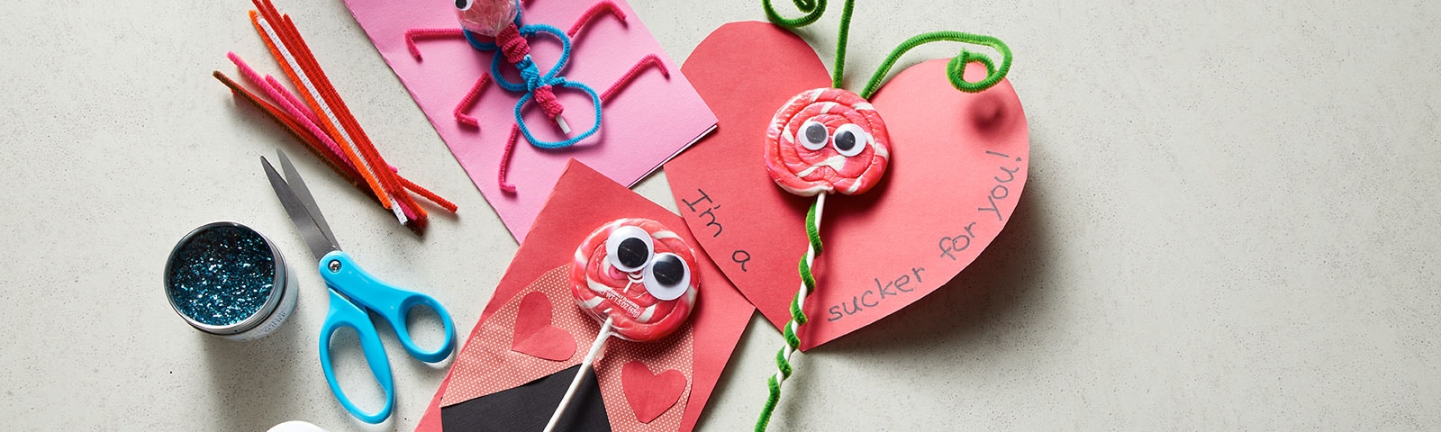 Table scattered with craft supplies and three homemade valentine's cards fashioned as bugs with candy as the main component Table scattered with craft supplies and three homemade valentine's cards fashioned as bugs with candy as the main component