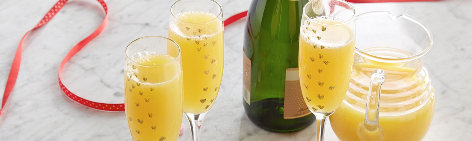 Crafty champagne flutes filled with mimosas in the foreground and candy hearts scattered on a marble countertop Crafty champagne flutes filled with mimosas in the foreground and candy hearts scattered on a marble countertop