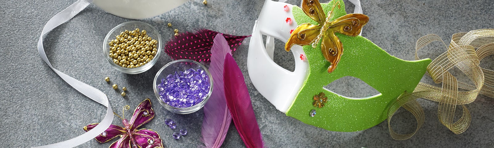 Two decorated Mardi Gras masks next to bowls of beads and ribbon strewn about