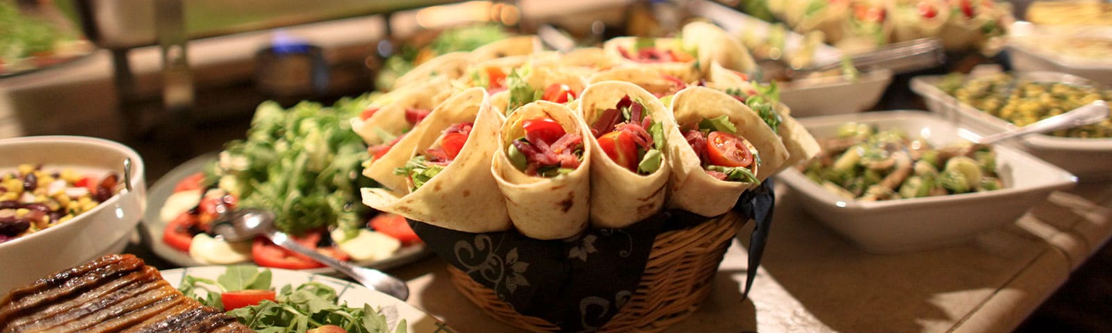 a bountiful feast of wraps, greens and pasta salads sit on a long countertop a bountiful feast of wraps, greens and pasta salads sit on a long countertop